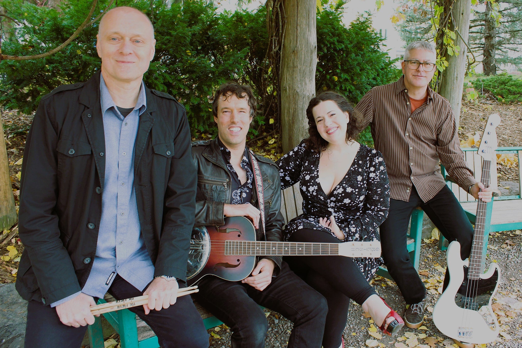 LH Express band members sitting outside on a bench in the Fall. Members include three men and one woman, who appear to be in their 40s-50s.