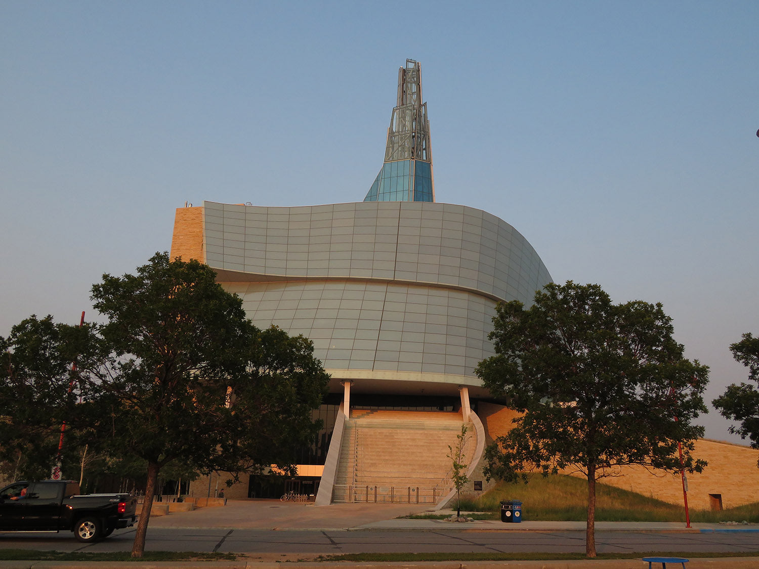 A view of the Canadian Museum for Human Rights building from between two trees, at sunset 
